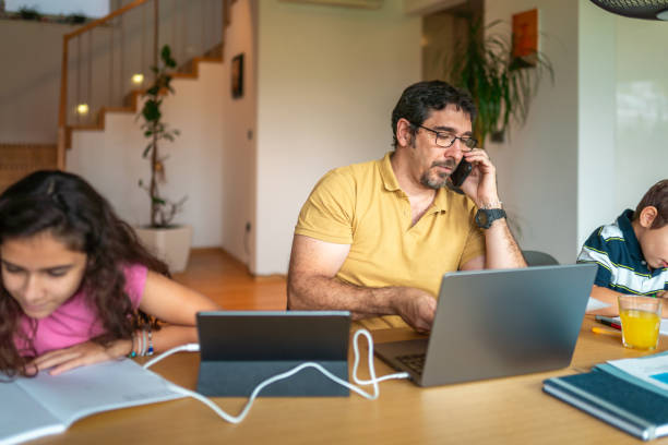 istock Mid Adult Hispanic Father Engaged in Remote Work Assisting Children with Studies 2190541047