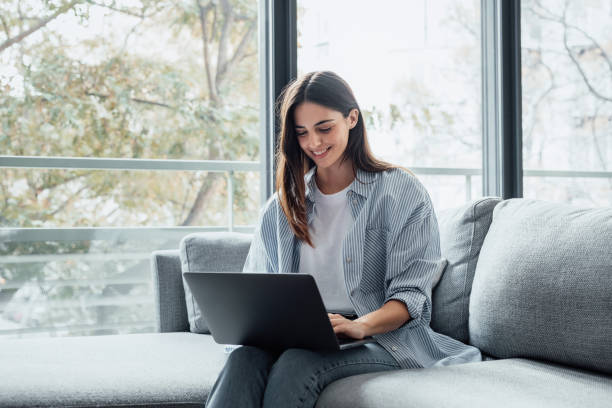 istock Concentrated millennial girl sit on couch working on laptop browsing internet at home during lazy weekend, focused young woman freelancer busy using computer surfing wireless web shopping online 2190548716