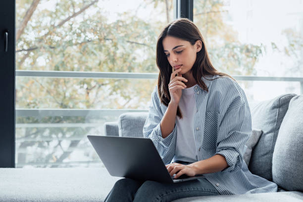 istock Concentrated millennial girl sit on couch working on laptop browsing internet at home during lazy weekend, focused young woman freelancer busy using computer surfing wireless web shopping online 2190549381