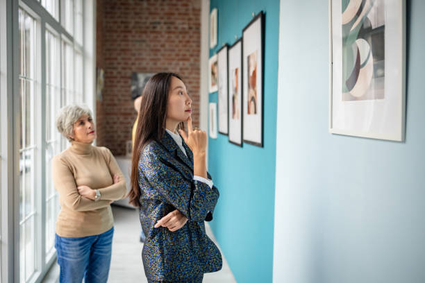istock Art gallery visitors admiring displayed pictures while curator observes attentively 2190550084