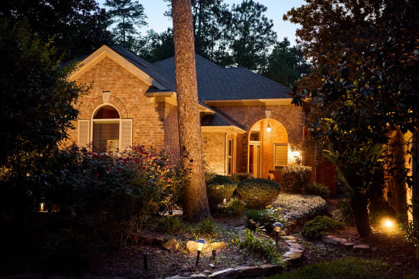 Exterior of a lovely stone and brick house surrounded by trees and a flourishing garden at night
