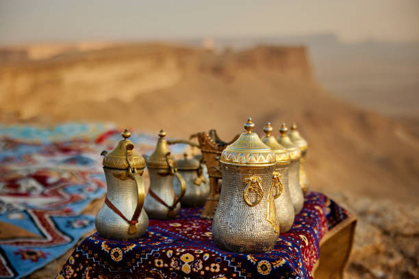 Traditional Arabic dallah coffee pots on cliff table at edge of the world, Riyadh Traditional Arabic dallah coffee pots arranged on a richly patterned fabric set against a stunning desert landscape at Edge of the World near Riyadh table ledge stock pictures, royalty-free photos & images
