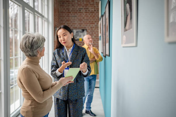Art gallery scene featuring a curator discussing pieces with attendees. The curator appears focused as visitors engage with artwork and the environment. The setting combines artistic expression and interactive learning.