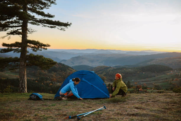 Mom and daughter spending a day in nature, going for a hike or a trail running exercise with their pet dogs. They are setting up a camping tent, ready to spend the night in the beautiful outdoors.