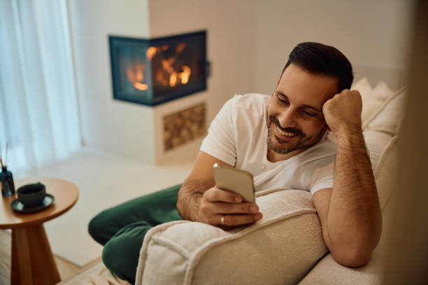 istock Happy man texting on cell phone while relaxing on the sofa. 2190557011
