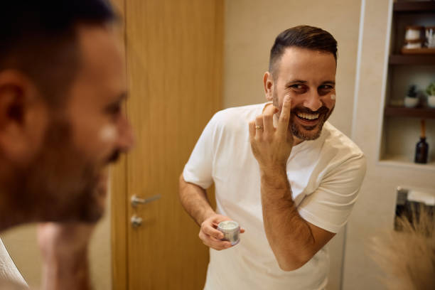 istock Reflection in a mirror on happy man using face cream in the bathroom. 2190557072