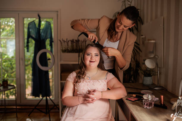 Loving big sister helps her younger sibling with Down syndrome prepare for prom night. She is doing her hair.