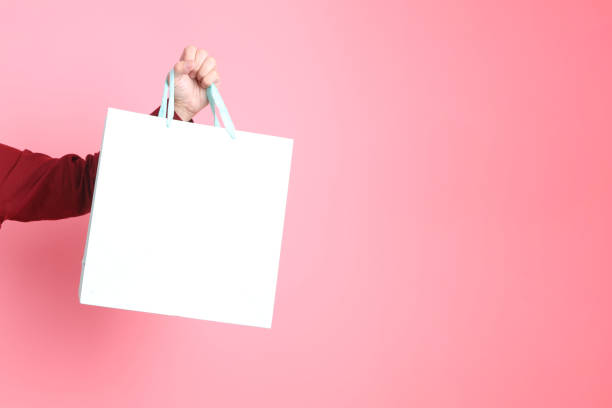 asian senior man in formal and casual red shirts with gesture of hand holding light blue polkadot shopping bag isolated on pink background.