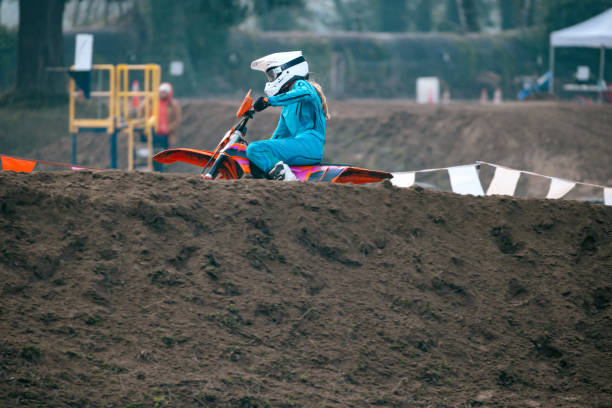 A Caucasian teenager partakes in women's motocross racing, speeding through laps on a track with jumps and berms.  Shot in Washington state, USA.