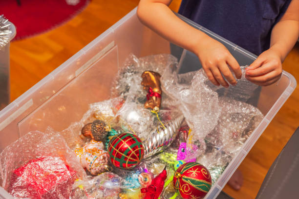 Child's hands carefully handling bubble pack over colorful Christmas ornaments in plastic storage box. Sweden.