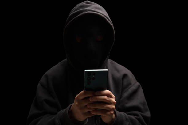 istock Hacker in black hood holding a cellphone, Scam cyber crime concept 2190582508