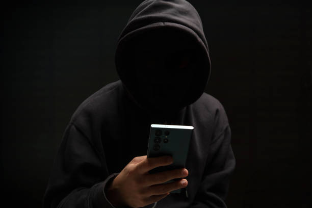 istock Hacker in black hood holding a cellphone, Scam cyber crime concept 2190582516
