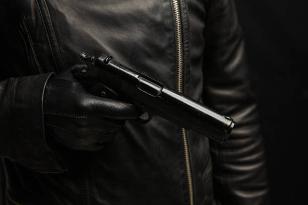 istock Armed man holding a gun closeup, criminal with leather gloves on dark background. 2190582521