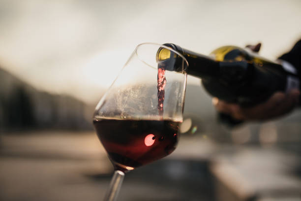 red wine being poured into glass at sunset outdoor setting - bottiglia di vino immagine foto e immagini stock
