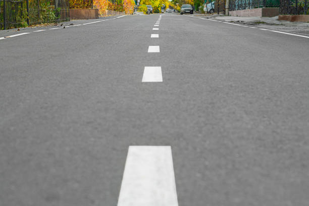 istock Asphalt surface with white dividing strip in the middle with perspective running along a street with country houses from a low angle. Road Leading to Future, an Abstract Symbol, a Concept of Movement 2190586518