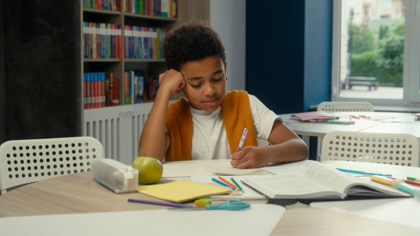 istock School classroom studying African American kid little boy son schoolboy pupil learner student tired sleepy child yawning learn lesson boring homework write test exam at desk study primary education 2190593675