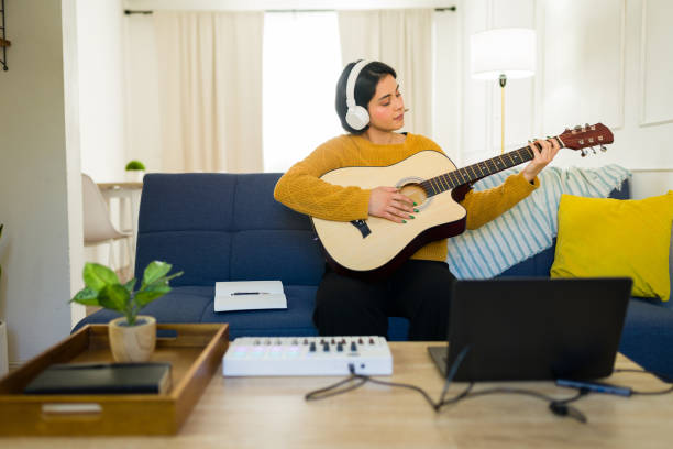 istock Beautiful young woman recording music playing guitar and using a midi controller at home in her living room 2190600701