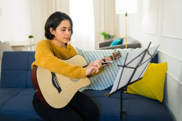 istock Focused young woman practicing guitar chords at home, using a music stand to follow notes and improve musical skills 2190600780