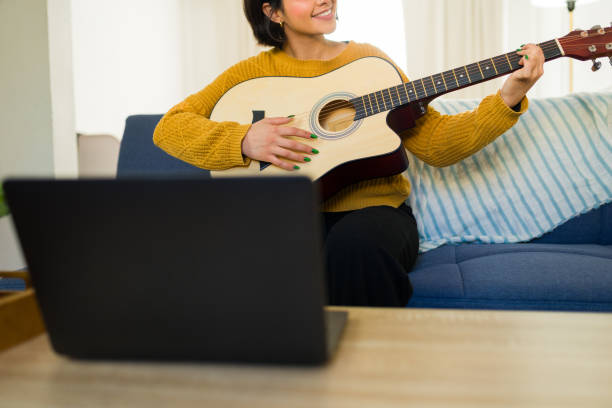 istock Young woman practicing guitar using an online lesson on her laptop, enjoying music learning in her living room 2190600793