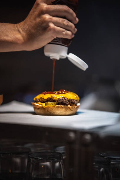 Chef pouring ketchup on a delicious burger in a restaurant kitchen