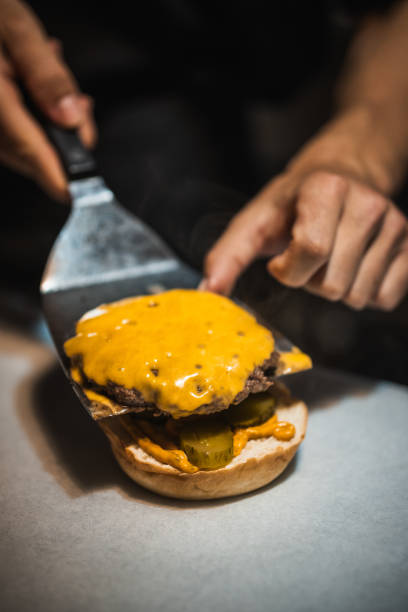 istock Chef placing cheeseburger patty on bun with spatula in restaurant kitchen 2190604587