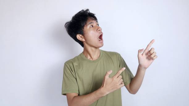istock young asian man shocked looking and pointing to the left side 2190604702