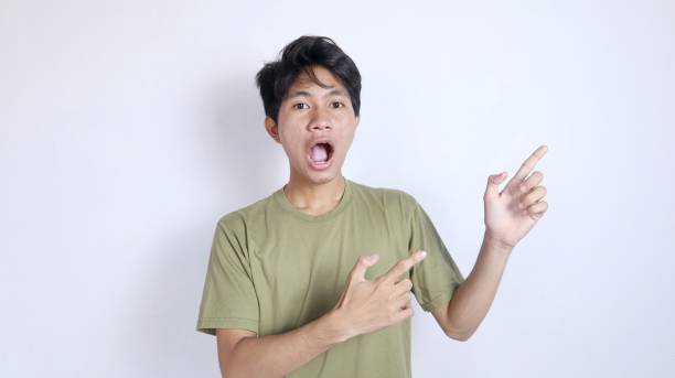 istock young shocked asian man looks forward and points to the left side 2190604706