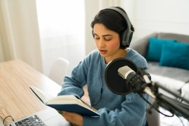 istock Content creator immersed in reading a book while recording audio for her engaging online podcast channel in a cozy home studio setting 2190607218
