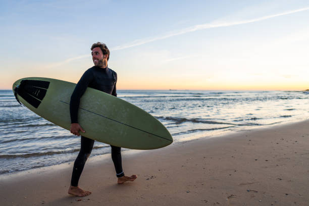 istock Surfer with Board Walking on Beach at Dusk 2190607294
