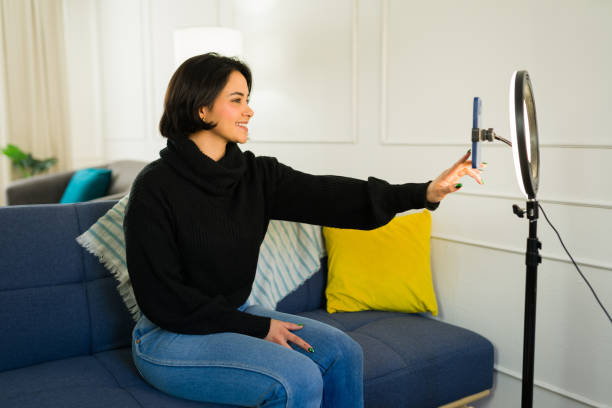 istock Young latina creator vlogging with smartphone, ring light, seated on home living room sofa, producing online content 2190607621