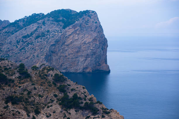 High cliffs jutting out far into the sea. Beautiful seascape. Calm blue sea and clear sky above huge cliffs.