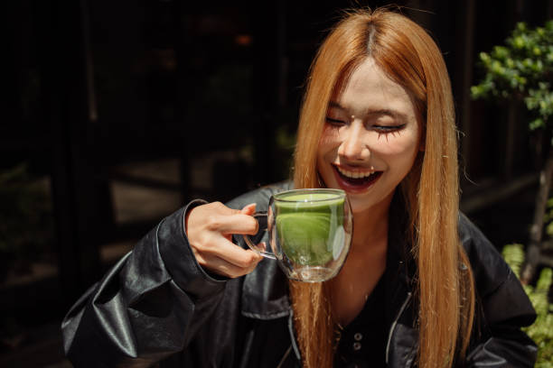 A smiling young woman savoring a cup of matcha tea outdoors.