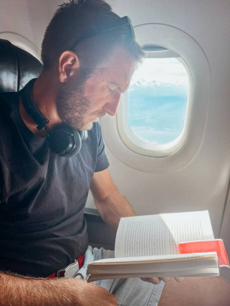 istock Man Reading a Book on Airplane Near Window 2190620441