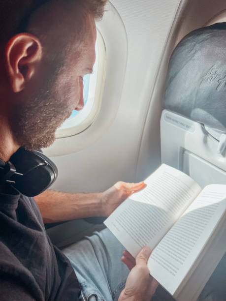 istock Man Reading a Book on Airplane Near Window 2190620445