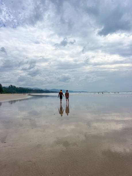 istock Two People Walking on a Tranquil Beach Under Cloudy Skies 2190622386
