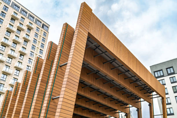 Modern wooden architectural design of outdoor stage with stacked beams and open spaces against a residential buildings and cloudy blue sky. Concept of contemporary architecture
