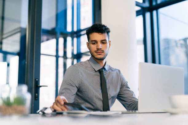istock Focused Young Professional Man Working at a Modern Office Desk with Laptop 2190639089