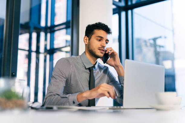 istock Young Professional Man Working in Modern Office on Laptop While Speaking on Phone 2190639097