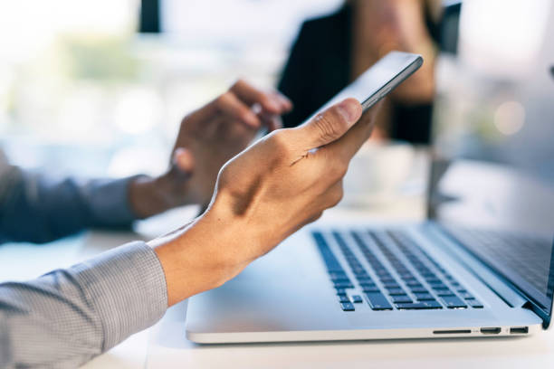 Close-Up Of Hands Using Smartphone And Laptop In Modern Office Setting