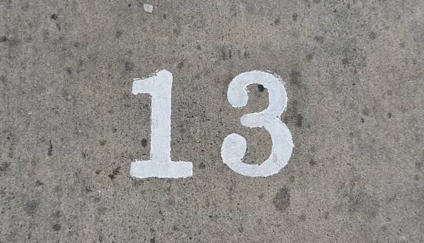 The concrete road surface has numbers. The parking area is dark grey, old, dirty, and has letters. White numbers are painted on the grey road surface. Number 13
