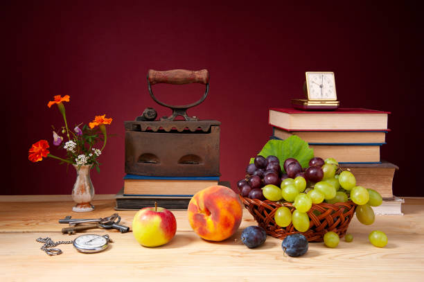 Still life, old clothes iron, books, alarm clock and fruit on a wooden table
