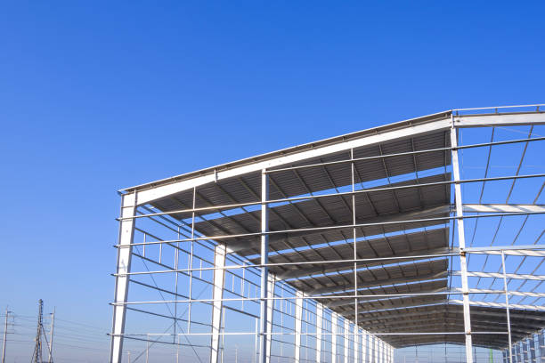 istock Industrial warehouse factory building framework structure during install corrugated steel roofing work in construction site against blue sky background 2190647995