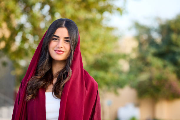 Portrait of smiling Saudi woman with red dupatta on her head. Young middle eastern female with long hair. She is representing Arab culture.