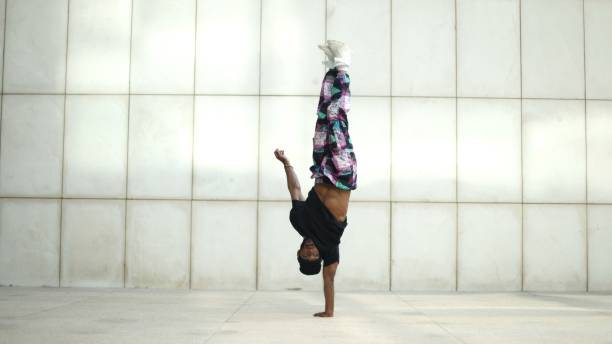 istock Young man breakdancing upside down, balancing on one hand in front of a white wall 2190650524