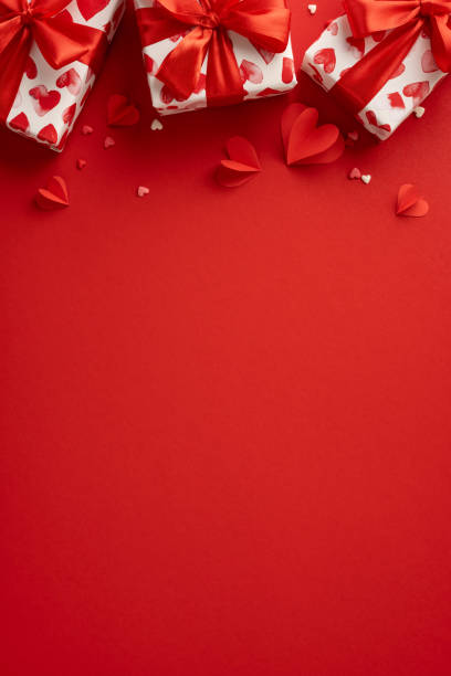 istock Romantic Valentine's Day vertical scene featuring heart-patterned gift boxes with red ribbons on a vibrant background 2190654252