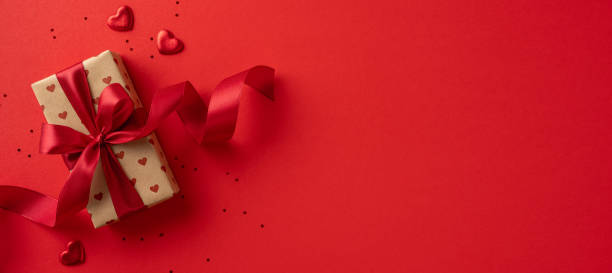 istock A beautifully wrapped gift with a red ribbon sits on a red background, accompanied by heart shapes, conveying love and romance for Valentineâs Day. 2190654304