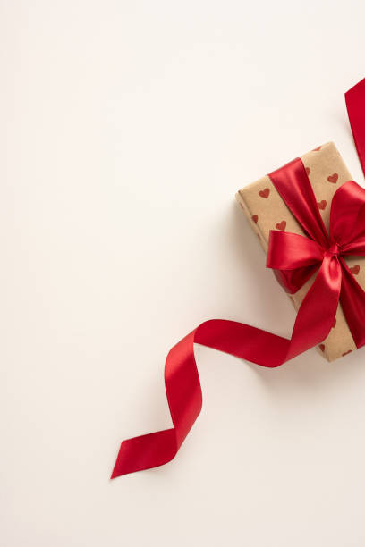 A vertical beautifully wrapped gift box with heart-patterned paper and a red ribbon. This image captures the essence of love, perfect for Valentine's Day or any special occasion