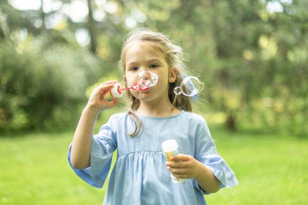 istock Little girl blowing soap bubbles in a green park 2190656150
