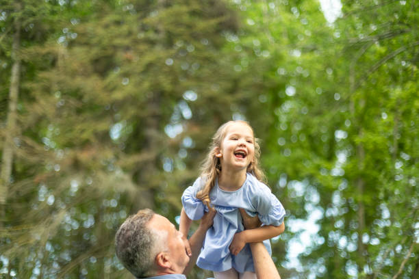 istock Father lifting laughing daughter in wooded park 2190656183