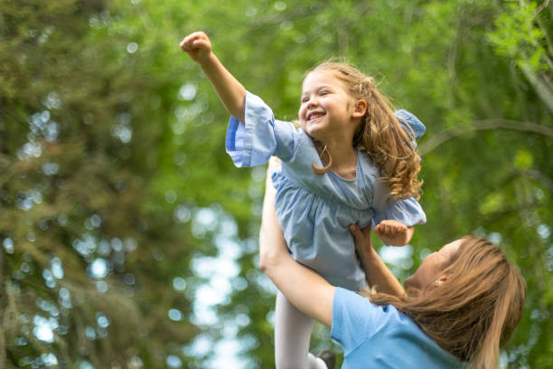 Mother lifting daughter in the air, playing superhero in a green park Happy mother lifting her cheerful daughter in the air, playing superhero in a green park, enjoying a sunny summer day superhero environment women green color stock pictures, royalty-free photos & images